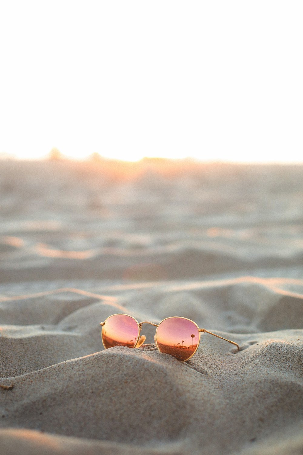 Óculos de sol redondo com lente espelhada rosé na areia